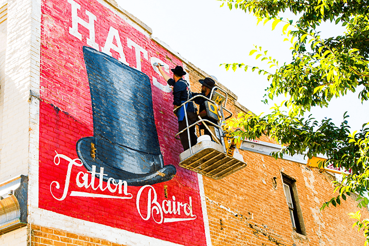 Colt Bowden and Josh Longoria painting the new classic style advertisement on the east side of the building.