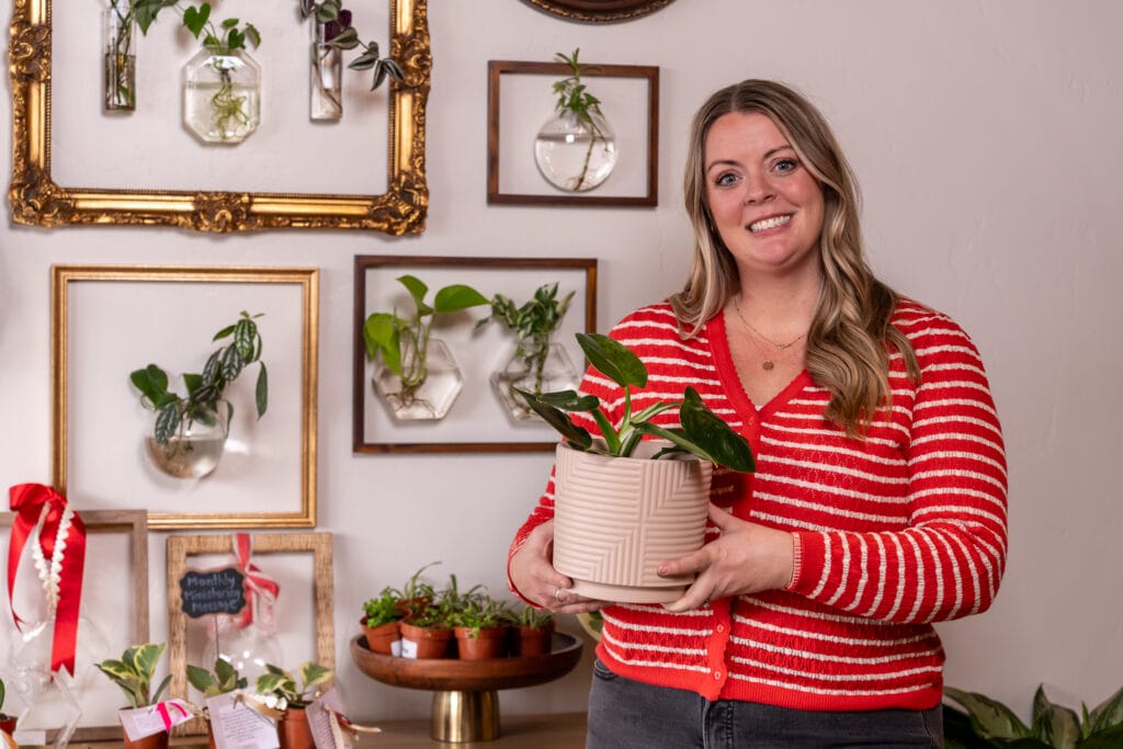Kellie Lee stands beside the beautifully arranged display of plants wall. 